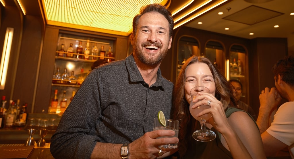 A smiling couple enjoys handcrafted cocktails in the warm, inviting atmosphere of the Boulevard Lounge.