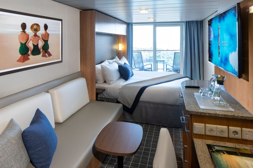 A modern, stylishly appointed AquaClass® stateroom featuring a private veranda, king-size bed, and comfortable seating area.