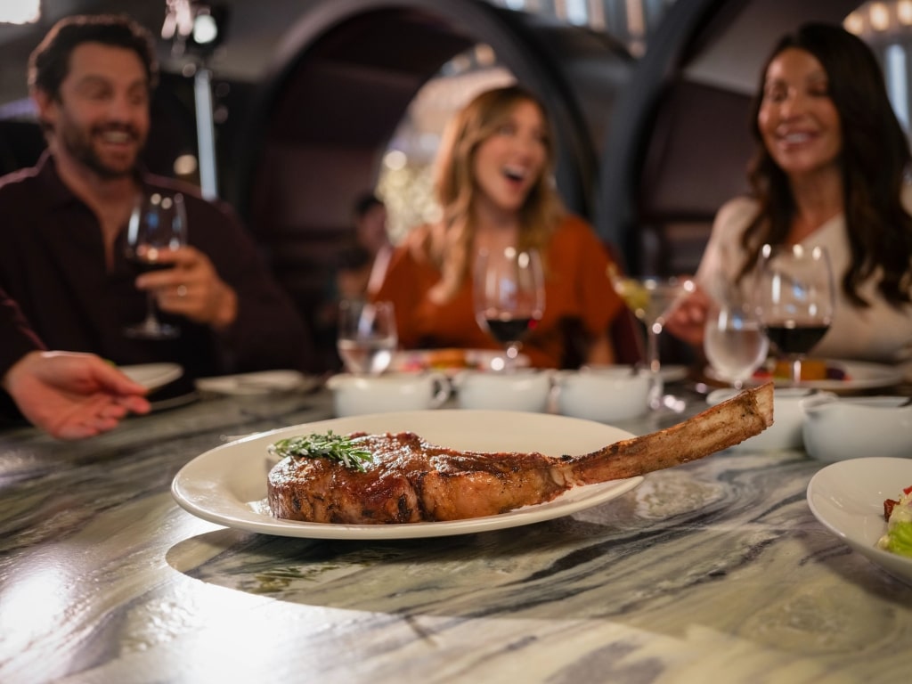 Guests enjoy fine dining over a grilled tomahawk ribeye steak at Fine Cut Steakhouse aboard Celebrity Cruises.