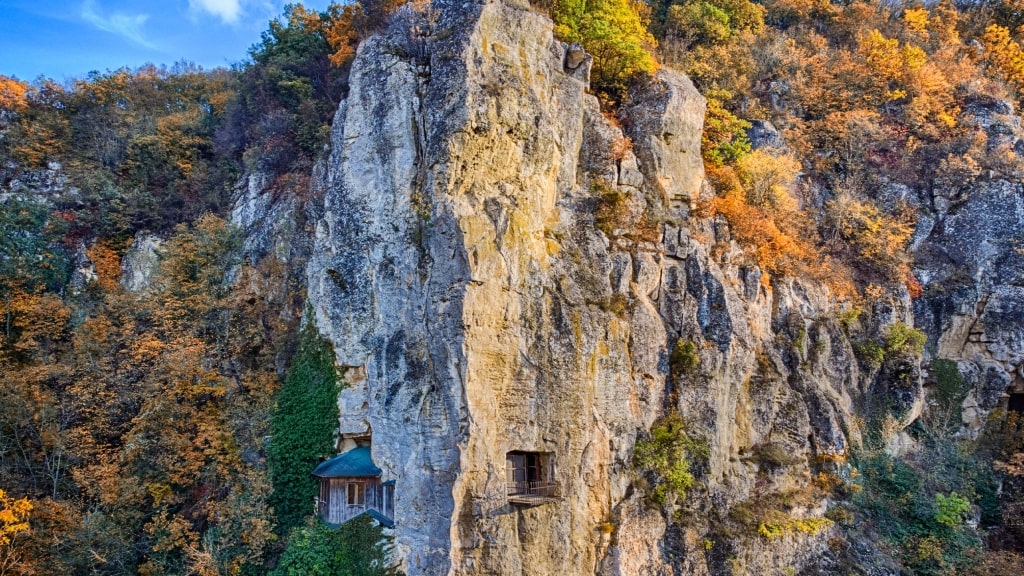 Ancient rock-hewn chambers cling dramatically to sheer limestone cliffs in autumn.