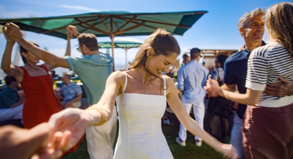 Guests dance hand-in-hand under bright green umbrellas in the lively, open-air setting of Sunset Park.
