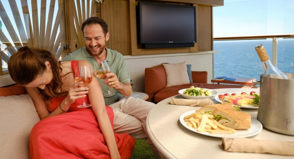 A laughing couple clinks wine glasses over an al fresco bistro meal with sweeping ocean views at Sunset Park Cafe.
