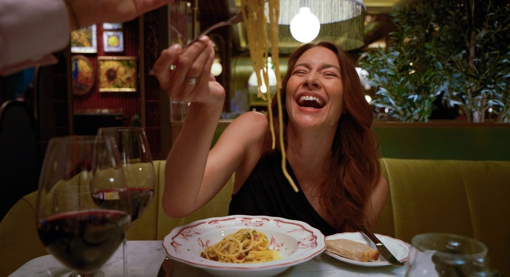 A guest laughs joyfully as fresh pasta is served tableside in the warm, intimate setting of Trattoria Rossa.