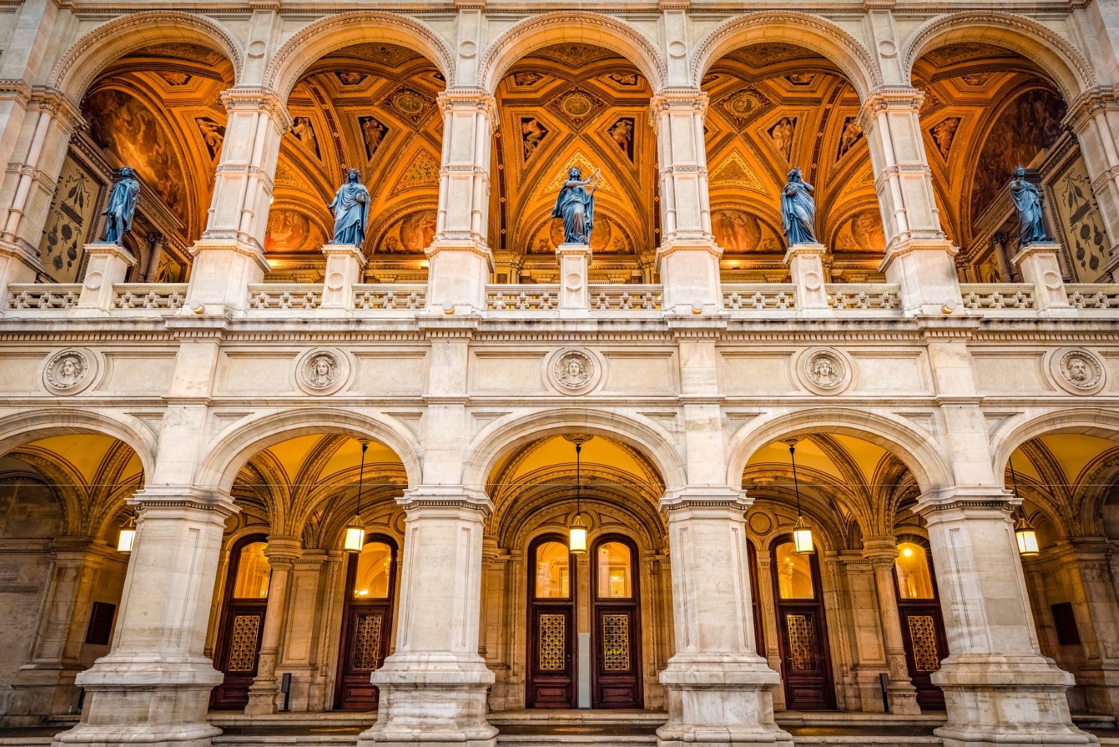 The grand Renaissance Revival facade loggia of the Vienna State Opera (Wiener Staatsoper), featuring illuminated stone arches and bronze statues representing the virtues
