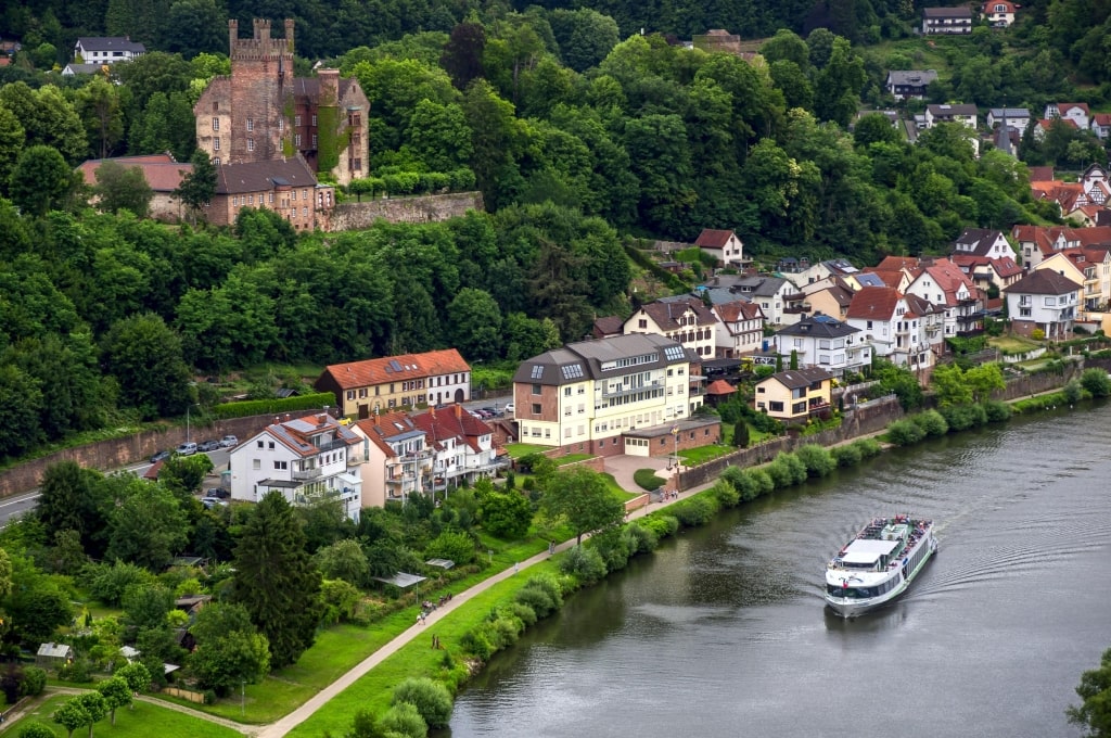 An aerial view of Mildenburg Castle (Schloss Mildenburg) perched on a wooded hill overlooking the Main River and a passing cruise boat.