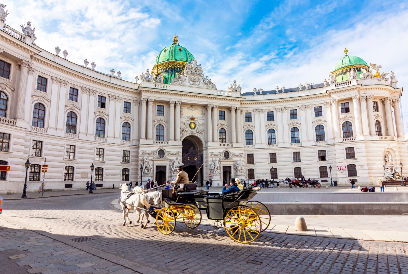 Traditional horse-drawn carriage (Fiaker) passing in front of the Michaelertrakt facade and dome of the Hofburg Palace at Michaelerplatz