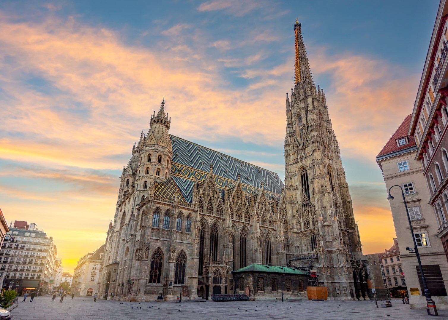 The Gothic Stephansdom (St. Stephen's Cathedral) with its ornate tiled roof and soaring south tower against a warm sunrise sky