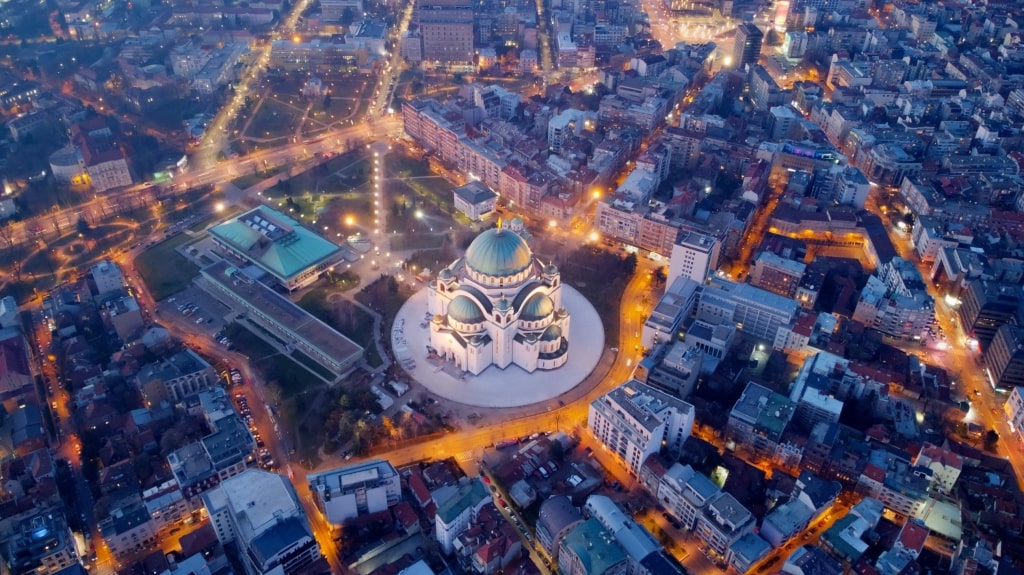 An aerial night view of the illuminated Church of Saint Sava surrounded by glowing city streets.