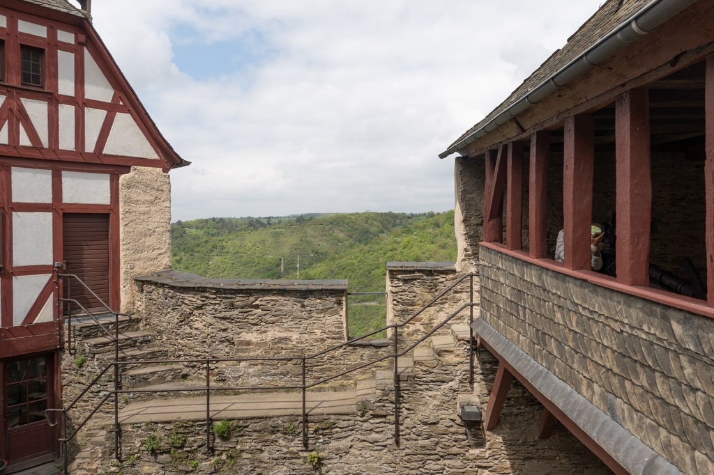 A view from inside the upper courtyard and stone fortifications of the historic Marksburg Castle, looking out over the surrounding hills of the Rhine Valley.