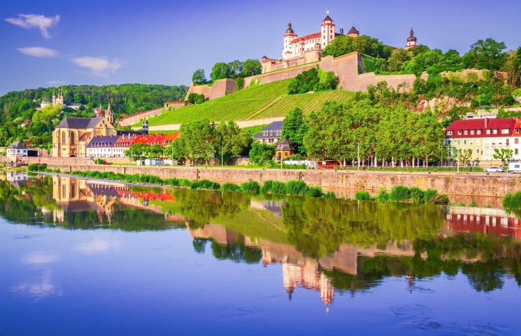 The Marienberg Fortress (Festung Marienberg) perched atop vineyard slopes, reflecting clearly on the calm waters of the Main River in Würzburg.