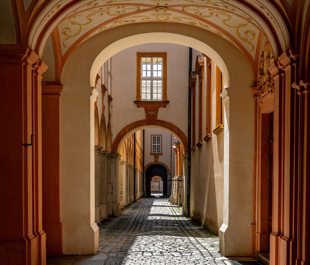 Sunbeams filter through vaulted arches along the historic stone path at Melk Abbey.