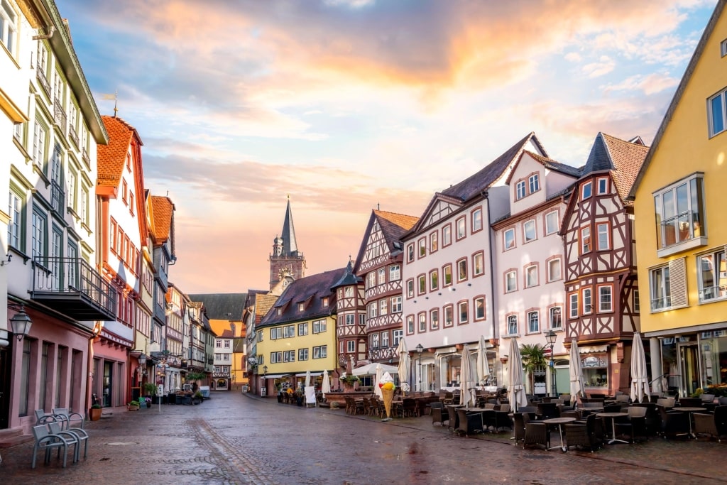 Historic half-timbered buildings surrounding the cobblestone Market Square (Marktplatz) at sunset, with the spire of the Stiftskirche in the background.