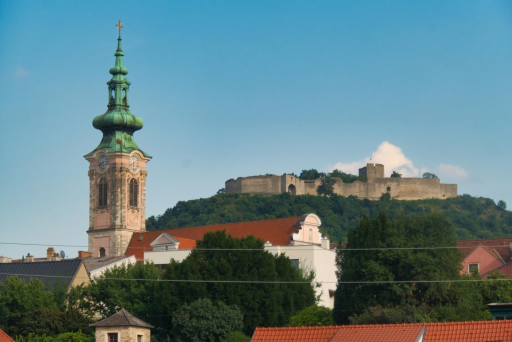 Perched dramatically on the hill above Hainburg, historic castle ruins overlook the town, with a tall church spire rising in the foreground.