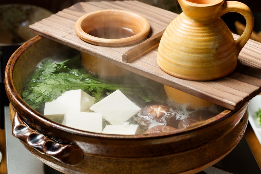 Traditional Japanese yudofu (boiled tofu hot pot) served with fresh vegetables and warm ponzu dipping sauce in an earthenware donabe pot.