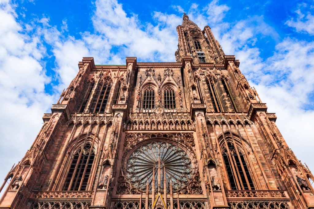The intricate, pink sandstone west facade and soaring single spire of Strasbourg Cathedral (Cathédrale Notre-Dame) against a bright blue sky.