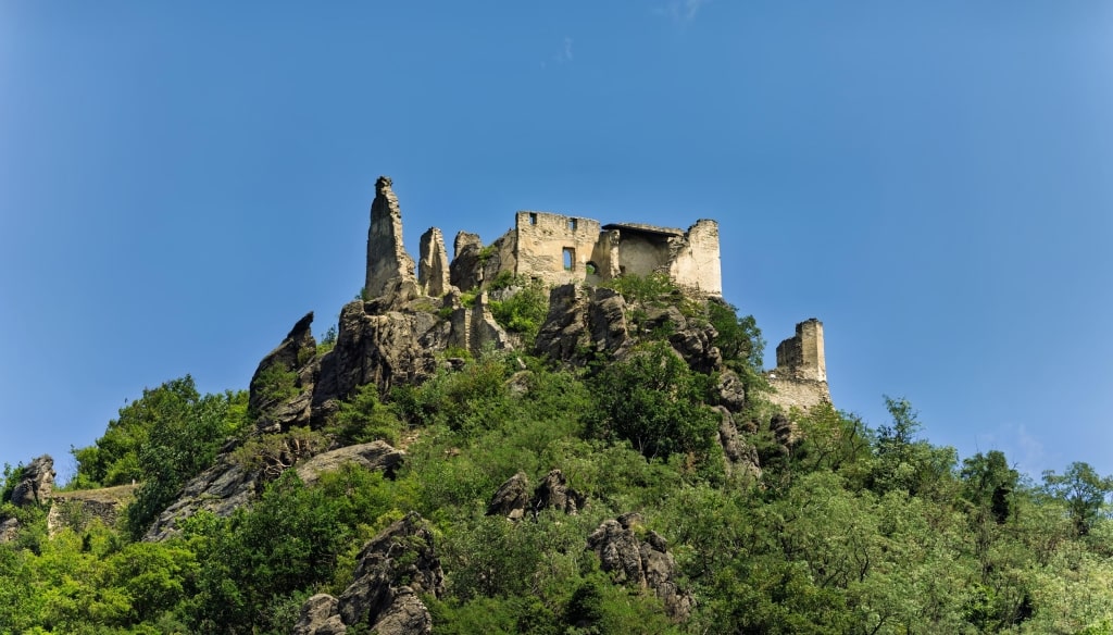 The medieval stone ruins of Dürnstein Castle perch dramatically atop a rocky, forest-clad hill against a clear blue sky.