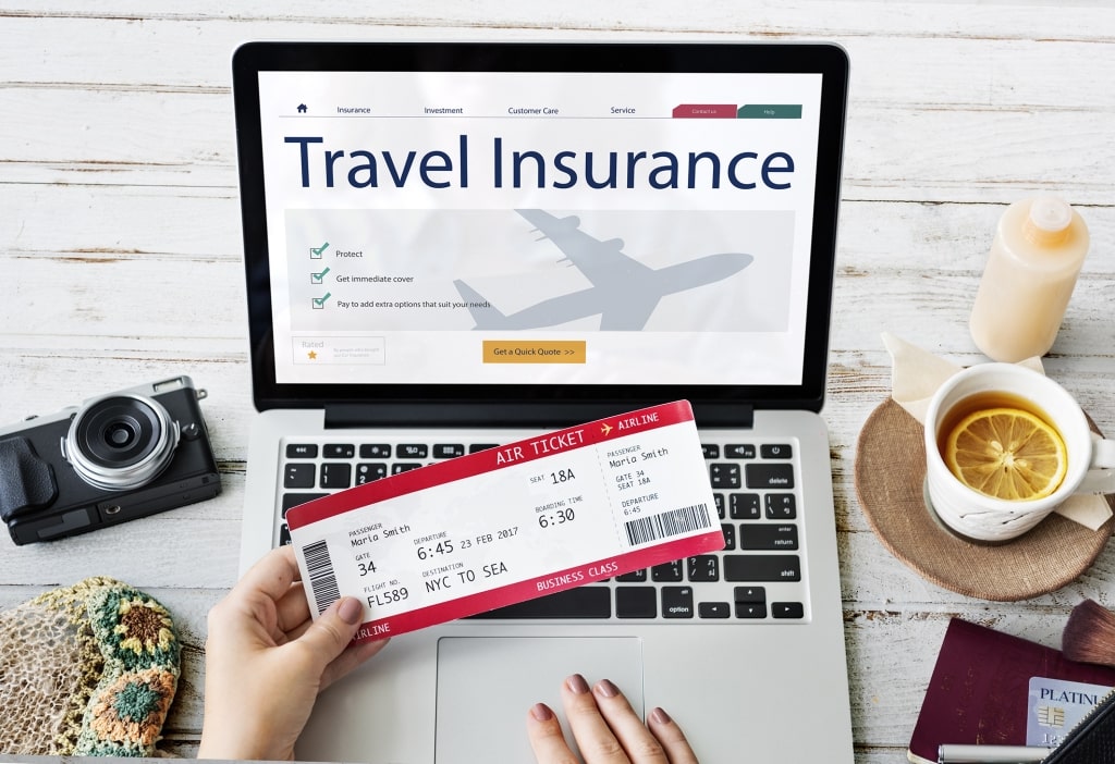 A traveler holds a red airline ticket over a laptop showing travel insurance options while preparing for an upcoming cruise.