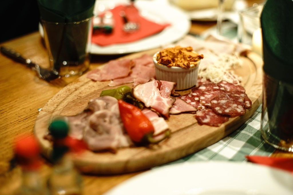 A traditional Austrian Brettljause served on a wooden board with cured meats, cold cuts, spreads, and pickled peppers.